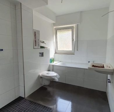 Badezimmer mit WC, Waschbecken und Badewanne, helle Fliesen und Fenster.