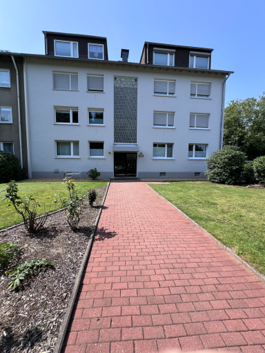 Eingang eines mehrstöckigen Wohngebäudes mit gepflastertem Weg und grünem Garten.