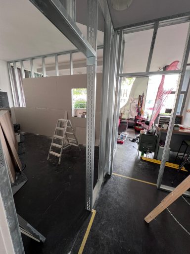 Baustelle mit Metallrahmen, Leiter und Halbfertigwand in einem Raum.